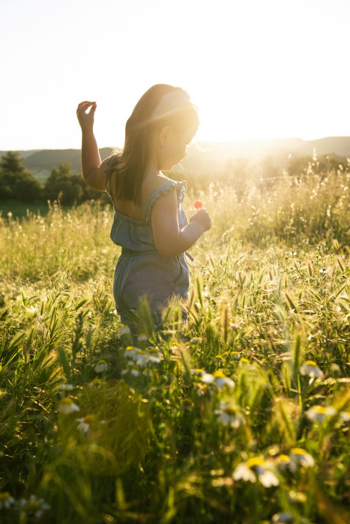Niña jugando en un campo de trigo verde con reflejos dorados por el sol