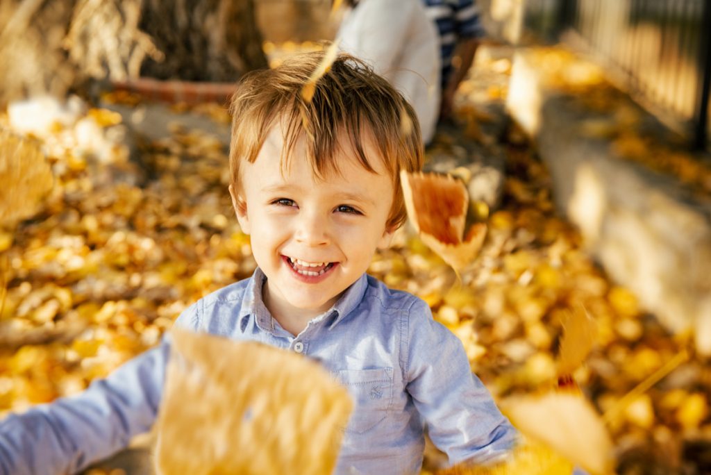 Niño sonriendo entre hojas otoñales naranjas